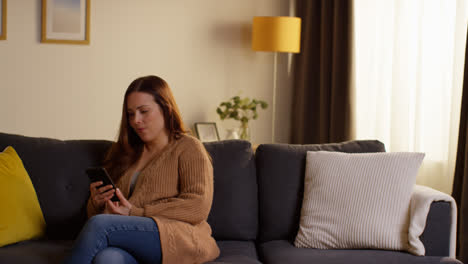 Woman-Sitting-On-Sofa-At-Home-At-Streaming-Or-Watching-Movie-Or-Show-Or-Scrolling-Internet-On-Mobile-Phone-2